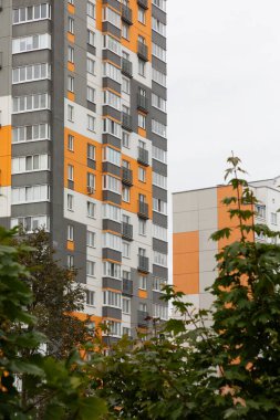 Modern yüksek katlı apartman binaları hareketli bir yerleşim bölgesinde yeşilliklerle çevriliyken canlı renkler sergiliyor. Bu evler kentsel yaşam seçeneklerini temsil ediyor..