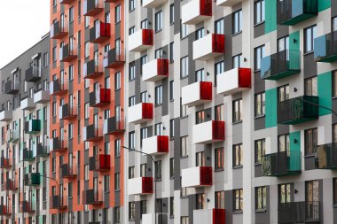 Çağdaş apartman binaları kalabalık bir yerleşim bölgesinde canlı yüzler ve balkonlar sergiliyor, kentsel yaşam seçeneklerini vurguluyor.