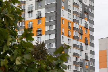 Canlı, yüksek katlı apartman binaları, ağaçların ve kentsel yaşamın arka planında cesur renkler ve modern tasarımla dolu bir yerleşim bölgesinde dimdik duruyorlar..