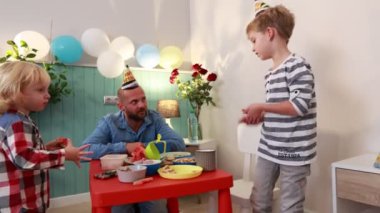 Bir baba ve oğlu, rengarenk dekorasyonlar ve pasta ve atıştırmalıklarla çevrili bir evde doğum gününü kutluyorlar. Neşe ve heyecan aşikar..