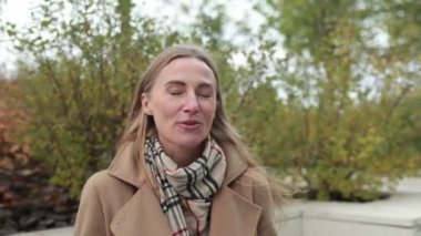 Bir kadın, sıcak bir palto ve eşarp giyerek canlı sonbahar yapraklarıyla dolu bir parkta dikilirken düşüncelerini ve deneyimlerini paylaşır..