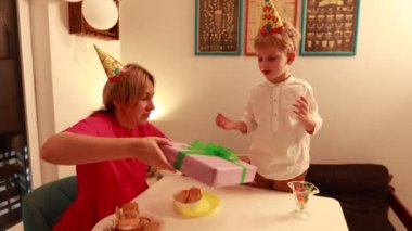 Neşeli bir anne, iki oğluyla birlikte kapalı bir alanda doğum gününü kutluyor. Hediyeleri açarken pastayı ve kahkahayı paylaşıyorlar..