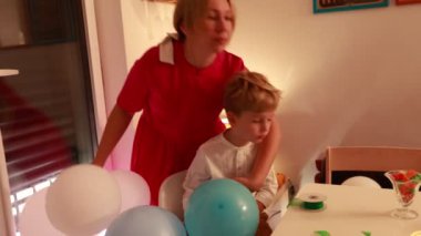 Neşeli bir doğum günü kutlaması başlıyor. Bir anne, evinde renkli balonlarla çevrili iki oğluyla samimi bir anı paylaşıyor..