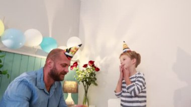 Bir baba ve oğlu doğum günü kutlaması için bir masada oturuyorlar. Parti şapkası takan çocuğun eli ağzında, muhtemelen bir dilek diliyor..