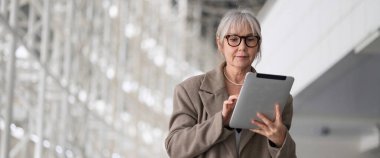 Orta yaşlı bir işkadını tabletine odaklanmış, aydınlık, çağdaş bir ofis ortamında çalışıyor..