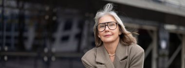 Üst düzey işkadını, güven ve profesyonellik yayarak çağdaş bir ofis binasının dışında poz veriyor..