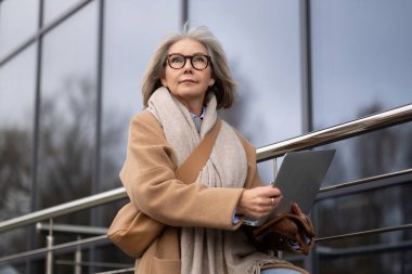 Son sınıf öğrencisi bir kadın, sıcak bir palto ve eşarp giymişti. Çağdaş camdan bir binanın dışındaki korkuluklara oturmuş, soğuk havada yaptığı işten zevk alırken bilgisayarına odaklanmıştı..