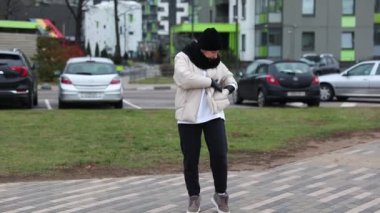 Çağdaş binalar ve çimen parçalarıyla çevrili bir otoparkta günlük kıyafetlerini giymiş biri geziniyor. Hava serin görünüyor, mevsimsel değişimleri gösteriyor..