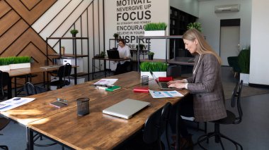 Parlak, çağdaş bir çalışma alanında, iki profesyonel duvarlardaki yeşil ve motivasyon alıntılarıyla çevrili büyük bir ahşap masada odaklanmış çalışmalara girişiyor..