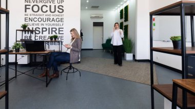 İki profesyonel, yaratıcılık ve ilham için tasarlanmış şık bir çalışma ortamında etkileşim halindeler. Duvardaki motivasyon ifadeleri üretkenlik atmosferini artırır.