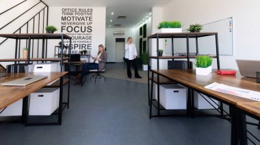 İki profesyonel, yoğun bir iş günü boyunca odak ve yenilikleri destekleyen, yeşillik ve işbirlikçi çalışma alanlarıyla dolu çağdaş bir ofis ortamında etkileşim halindedir..