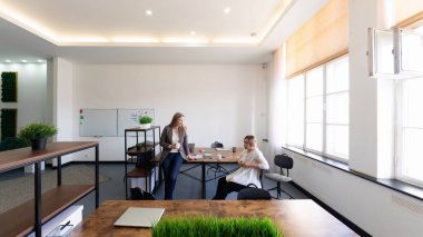 İki kadın, parlak ve modern bir ofis alanında ortak bir tartışmaya giriştiler. Açık alan yeşillik ve geniş doğal ışık içeriyor, yaratıcılığı ve takım çalışmasını teşvik ediyor..