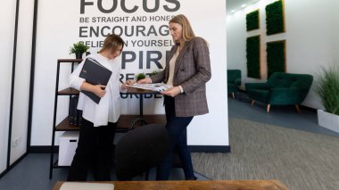 Çağdaş bir ofiste, iki kadın belgeleri incelerken bir tartışmaya girişirler. Alan yeşil dekor içerir ve takım çalışması ve ilham üzerine odaklanır.