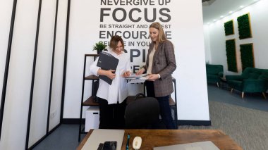 İki profesyonel, çağdaş bir ofiste duvarda yer alan motivasyon alıntılarıyla çevrili bir tartışmada yer alıyor. Belgeleri gözden geçirir ve parlak bir ortamda fikirleri paylaşırlar..