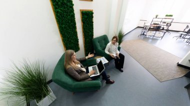 İki meslektaş şık bir ofis salonunda otururken bir tartışmaya girişirler. Bir kişi dizüstü bilgisayar kullanıyor ve diğeri aktif olarak dinliyor. Taze bitkiler canlı bir atmosfer sağlar..