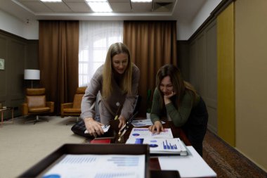 İki kadın, iyi aydınlatılmış bir ofis alanında ahşap bir masada işbirliği yaparken, grafikleri ve grafikleri analiz eden bir iş sunumuna odaklanmış durumdalar..