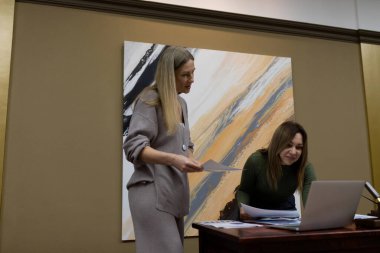 İki profesyonel, çağdaş bir ofiste dokümanlar ve bir laptop ekranı incelerken bir tartışmaya giriştiler. Arkaplan çalışma alanını geliştiren soyut sanat eserleri.