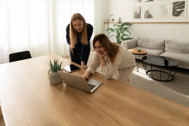 İki kadın, bitkiler ve rahat mobilyalarla çevrili, ahşap bir masada dizüstü bilgisayara yaslanarak verimli bir tartışmaya girişirler..