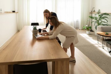 İki kadın, bitkilerle süslenmiş, geniş, aydınlık bir odadaki uzun tahta bir masanın üzerine dizüstü bilgisayar dayıyorlar. Tartışıyorlar, fikirlerini paylaşıyorlar..