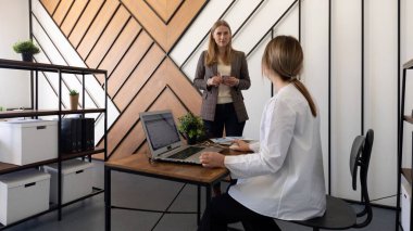 İki kadın şık bir ofis alanında profesyonel bir tartışmaya giriyorlar. Biri bir masada dizüstü bilgisayarla oturup ortak bir ortamda fikir alışverişinde bulunurken diğeri ayakta duruyor..