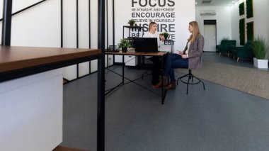 Motivasyonel alıntılar ve yeşilliklerle çevrili şık bir ofis çalışma alanında iki kadın bir tartışmaya girişiyor. Atmosfer yaratıcılığı ve işbirliğini teşvik eder..