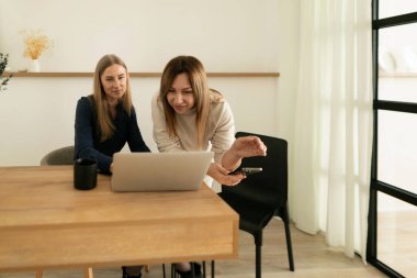 İki kadın, iyi aydınlatılmış bir çalışma alanındaki ahşap bir masada ortak bir tartışmaya giriştiler. Fikir alışverişinde bulunurken bilgisayardaki içeriği gözden geçirirler..