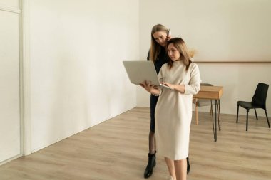 Şık, hafif bir çalışma alanında, iki kadın fikirleri tartışırken dizüstü bilgisayara odaklanıyor. Bir kadın diğerinin arkasında duruyor, ikisi de işine odaklanmış..