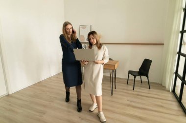 Minimalist bir ofiste yaratıcı bir tartışmaya giren iki kadın. Biri dizüstü bilgisayarı işaret ederken diğeri dikkatle dinliyor. Doğal ışık atmosferi güçlendirir..