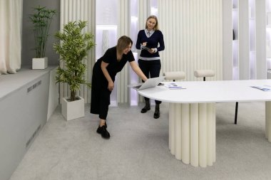 İki kadın şık bir ofis ortamında ortak bir tartışma içindeler. Bir kadın dizüstü bilgisayarın üzerine eğilirken diğeri not alıyor, ikisi de işine odaklanmış..