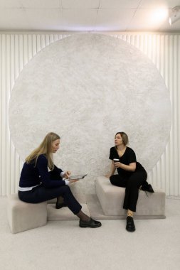 İki kadın çağdaş bir sanat ortamında canlı bir sohbete girişiyor. Biri notlar alırken diğeri minimalist bir alanda yaratıcılık ve işbirliği sergiliyor..