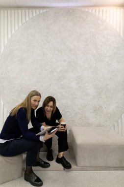 İki kadın, yaratıcılık için tasarlanmış çağdaş bir alanda otururken fikirler üzerinde işbirliği yapıyor. Kavrayışlarını paylaşıyorlar, ellerinde bir tablet ve içecek tutuyorlar, tartışmaya dalmışlar..