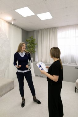 İki kadın doğal ışıkla dolu çağdaş bir ofiste sohbet ediyorlar. Belgeleri gözden geçirir, fikirleri paylaşır, işbirliği ve takım çalışması sergilerler..