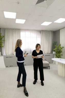 İki kadın, doğal ışıkla dolu çağdaş bir ofis alanında belgeleri tartışıyor ve inceliyor..