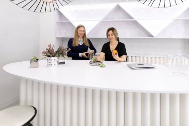 Çağdaş bir çalışma alanında iki kadın parlak, kıvrımlı beyaz bir tezgahta sohbet ediyorlar. Serinletici şeylerden hoşlanırlar ve şık dekorlarla çevrili sıcak, misafirperver bir atmosfer sergilerler..