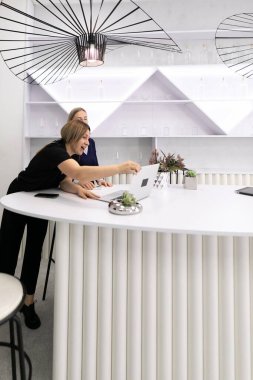 İki kadın, ilginç dekorlar ve yenilikçi aydınlatma donanımlarıyla çevrili çağdaş bir ofis alanında, şık bir beyaz masada ortak bir tartışmaya girişirler..