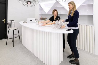 Çağdaş bir mekanda, iki kadın parlak beyaz bir tezgahta işbirliği yapar, çiçekleri düzenler ve tasarımları tartışırlar. Mekan, yaratıcı atmosferlerini geliştiren minimalist dekorlarla dolu..