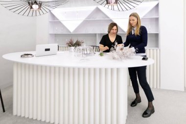 Çağdaş bir tasarım alanında, iki kadın dekoratif öğeleri düzenlemeye odaklanıyor..