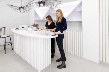 Şık, havalı bir mağazada, iki kadın şık bir perakende satış tezgahında ürünleri düzenlemeye odaklanıyor. Ayar, atmosferi geliştiren çağdaş tasarım elementleri ve nötr renklere sahiptir..