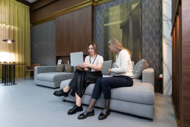 İki arkadaş şık bir salonda rahat bir kanepede oturup dizüstü bilgisayarla çalışırken fikirlerini paylaşıyorlar. Doğal güneş ışığı çağdaş uzayı aydınlatır.