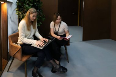 Çağdaş bir ofiste bitkiler ve sıcak aydınlatmalarla süslenmiş bir kadın, meslektaşı birlikte çalıştığı bir atmosferi gösteren bir kitabı incelerken dikkatle dizüstü bilgisayarına yazar..