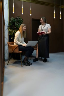 Çağdaş bir ofis ortamında iki kadın canlı bir tartışmaya girişiyor. Bir kadın elinde dizüstü bilgisayarla masada otururken, diğeri tabletle yanında duruyor ve fikirlerini paylaşıyor..