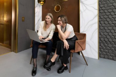 Çağdaş bir ofiste şık koltuklarda otururken iki kadın birlikte çalışırlar. Bir dizüstü bilgisayara odaklanmışlar, fikirleri tartışıyorlar..