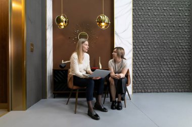 İki profesyonel kadın modern ofis ortamında şık dekorlu dokümanları incelerken sohbet ediyorlar. Ayar modern tasarım elementlerini yansıtır.