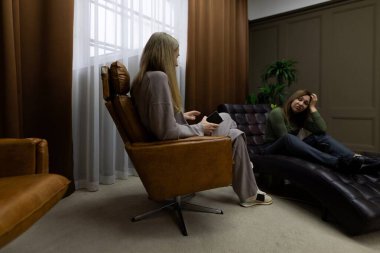 Ilık ve aydınlık bir odada, iki kadın derin bir sohbete tutulmuş rahat koltuklarda otururlar. Atmosfer sakin, açıklık ve güveni teşvik ediyor..