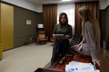 Çağdaş bir ofis ortamında iki kadın projeleri hakkında tartışıyorlar. Bir kadın tablet tutarken diğeri dikkatle dinliyor, fikirleri paylaşıyor..