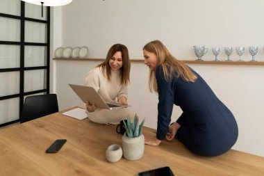 İki kadın, ahşap bir masanın üzerine dizüstü bilgisayarda ortak bir görev üstleniyorlar. Doğal ışık modern atmosferi geliştirir ve verimli bir ortam yaratır..