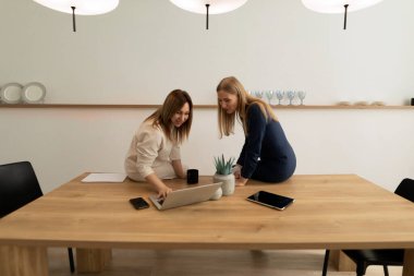 Çağdaş bir çalışma alanında, iki kadın fikirleri tartışırken bir dizüstü bilgisayara odaklanıyor. Bir bitki ahşap masaya taze bir dokunuş ekler, verimliliği ve işbirliğini artırır..