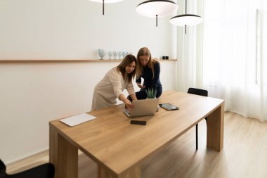 İki kadın, parlak ve modern bir çalışma alanında dizüstü bilgisayar üzerinde çalışırken ortak bir tartışmaya girişirler. Çevreleri yeşillik ve minimalist dekorlarla çevrili..