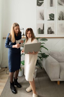 Çağdaş bir ofis ortamında iki kadın bir tartışma içindeler. Biri bir telefon tutarken diğeri şık dekorasyon ve yeşilliklerle çevrili bir dizüstü bilgisayara odaklanmış..