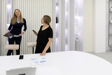 İki iş kadını, iş birliklerini ve üretkenliklerini artırmak için dijital cihazlardan ve belgelerden faydalanarak, şık bir ofis ortamında fikirleri tartışıyor..